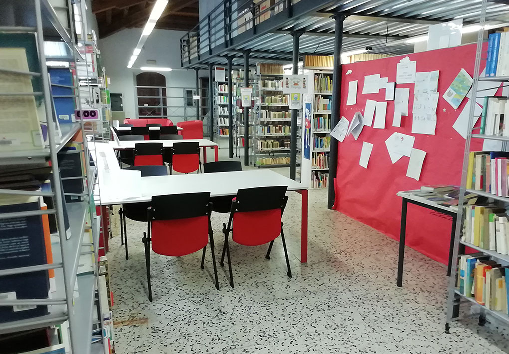 sala della biblioteca, con tavoli da consultazione a U e scaffali di libri