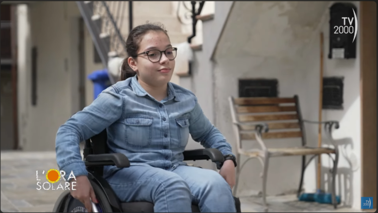 una schermata del video youtube. Una giovane ragazza in sedia a rotelle, sorridente.