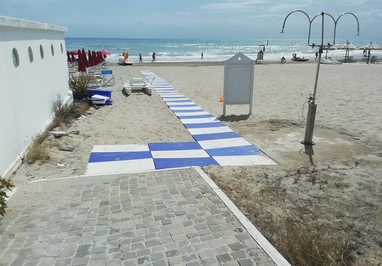 una spiaggia libera con passerella in plastica e doccia esterna