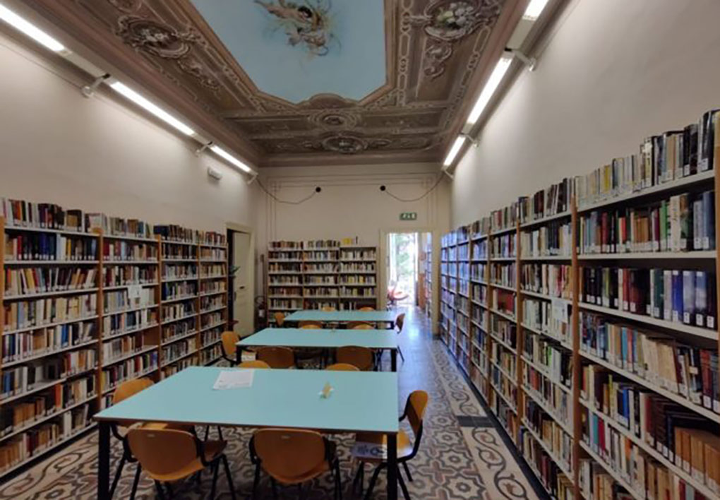 Una sala di biblioteca con scaffali ai lati, tavoli da lettura al centro e soffitti affrescati
