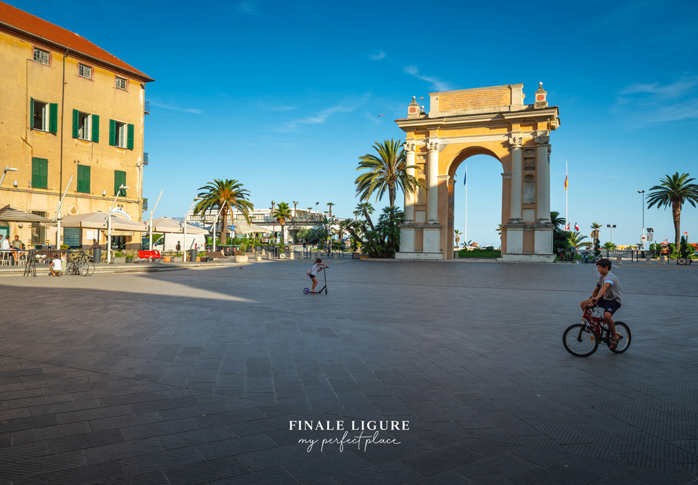 una piazza con, verso il mare, un arco monumentale