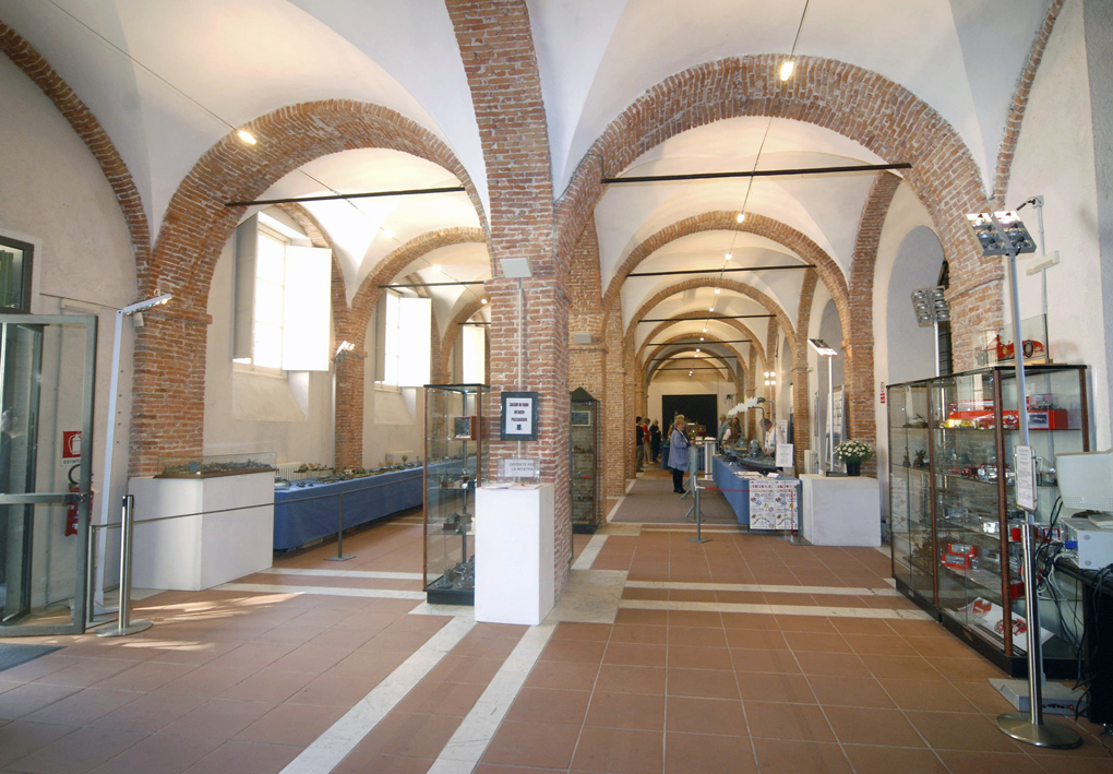 Una sala espositiva nel palazzo storico dove è stata allestita una mostra. Lo spazio è scandito regolarmente dalle colonne che reggono antiche volte a botte