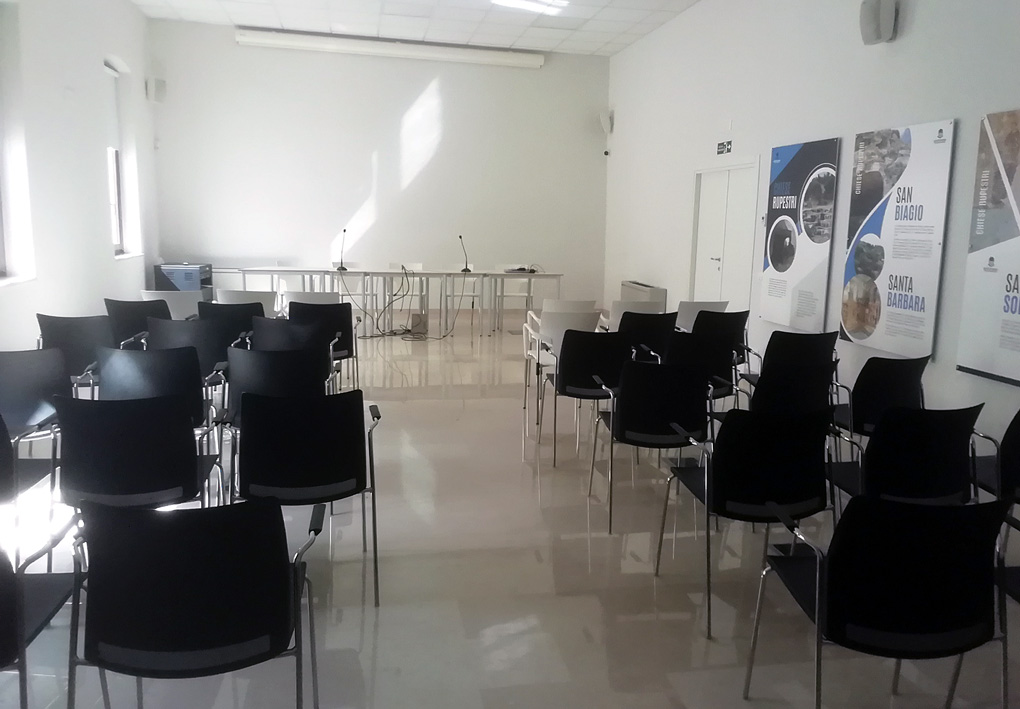 un'ampia e luminosa sala convegni, provvista di sedie in plastica e un tavolo per i relatori