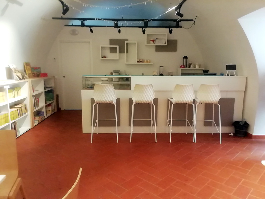 un moderno e accogliente bancone di un bar con sgabelli all'interno di un ambiente ricavato in un palazzo storico. Il soffitto è a volta e il pavimento in cotto contrasta piacevolmente con l'arredamento moderno.
