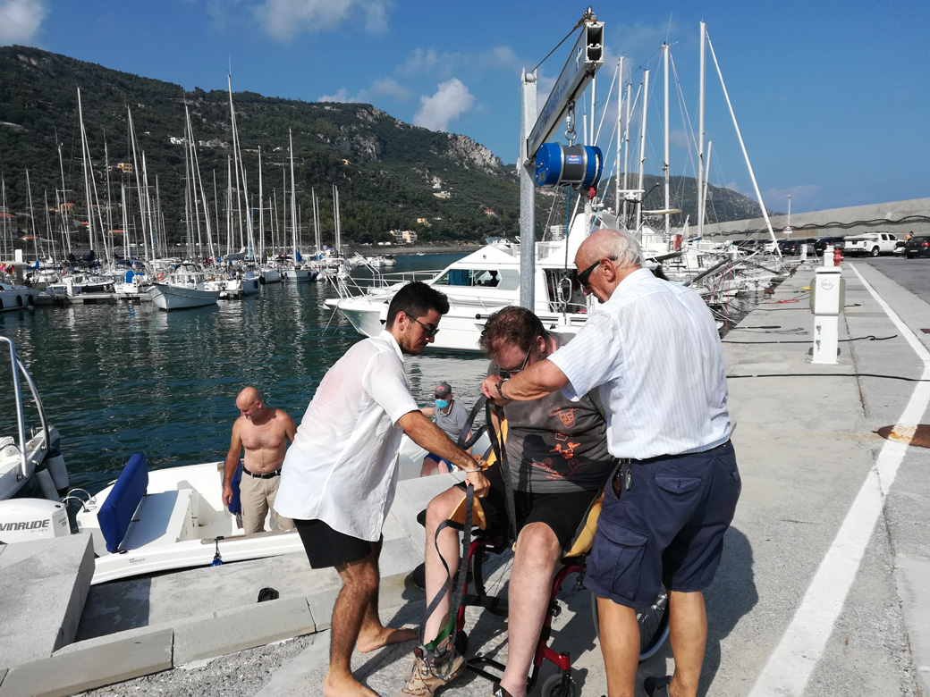 una persona in carrozzina viene aiutata a salire su una barca a vela