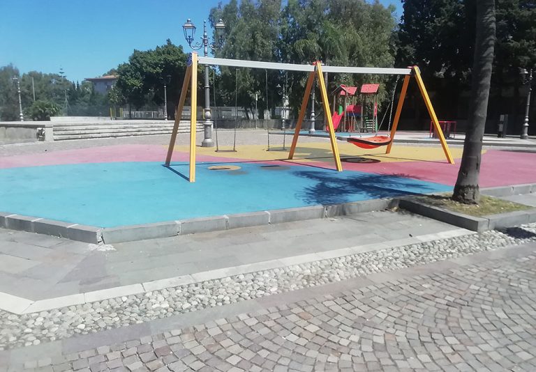un'altalena inclusiva in una'ampia piazza con alberi e giochi