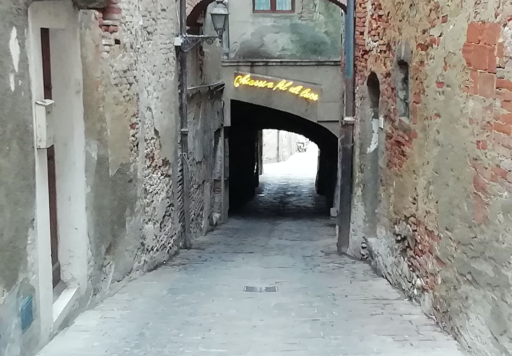 al di sopra di un passaggio tra palazzi, è appesa una scritta al neon