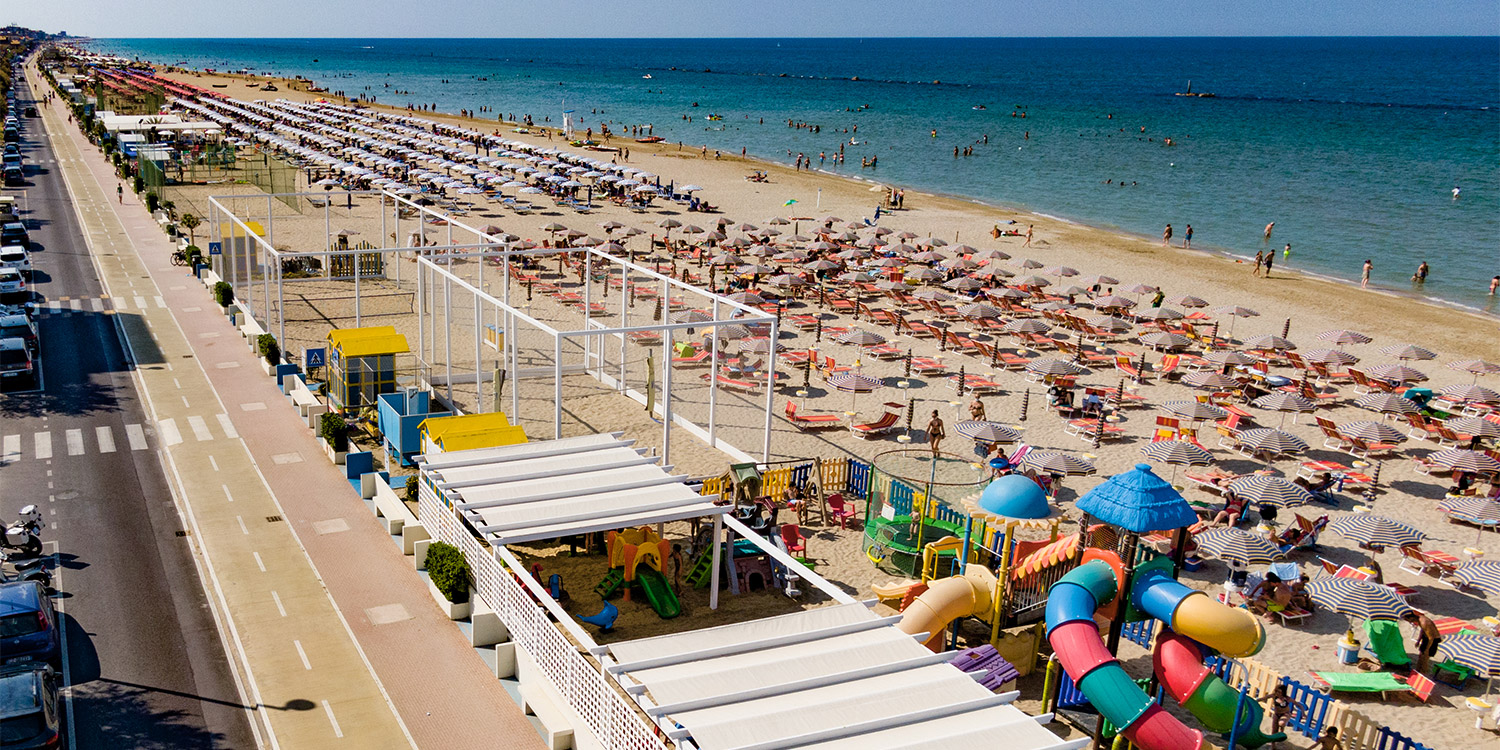 una lunga spiaggia sabbiosa piena di stabilimenti balneari con anche grandi strutture gioco per bambini