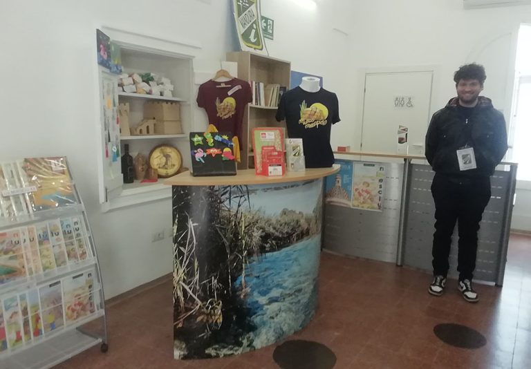 Un sorridente impiegato dell'infopoint accoglie le persone tra materiali promozionali
