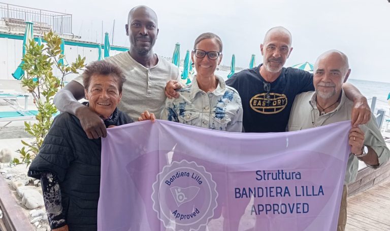 alt="Il presidente della Bandiera Lilla consegna il marchio Bandiera Lilla Approved ai gestori e allo staff dello stabilimento"