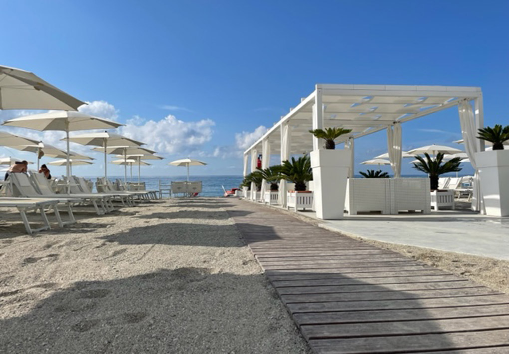 una passerella sulla spiaggia tra file di lettini e gazebi