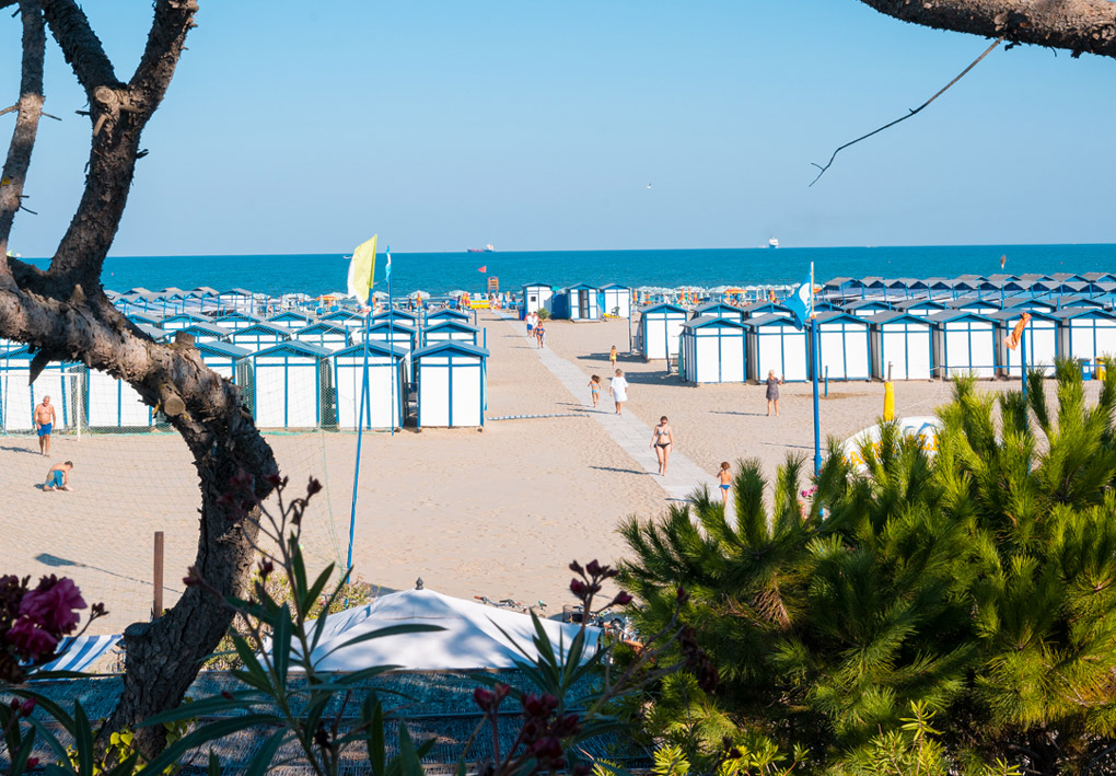 una lunga spiaggia sabbiosa con ordinate cabine e file di ombrelloni