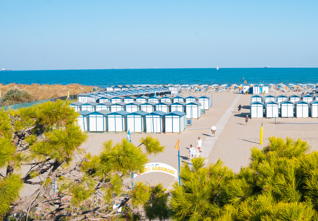 una lunga spiaggia sabbiosa con ordinate cabine e file di ombrelloni