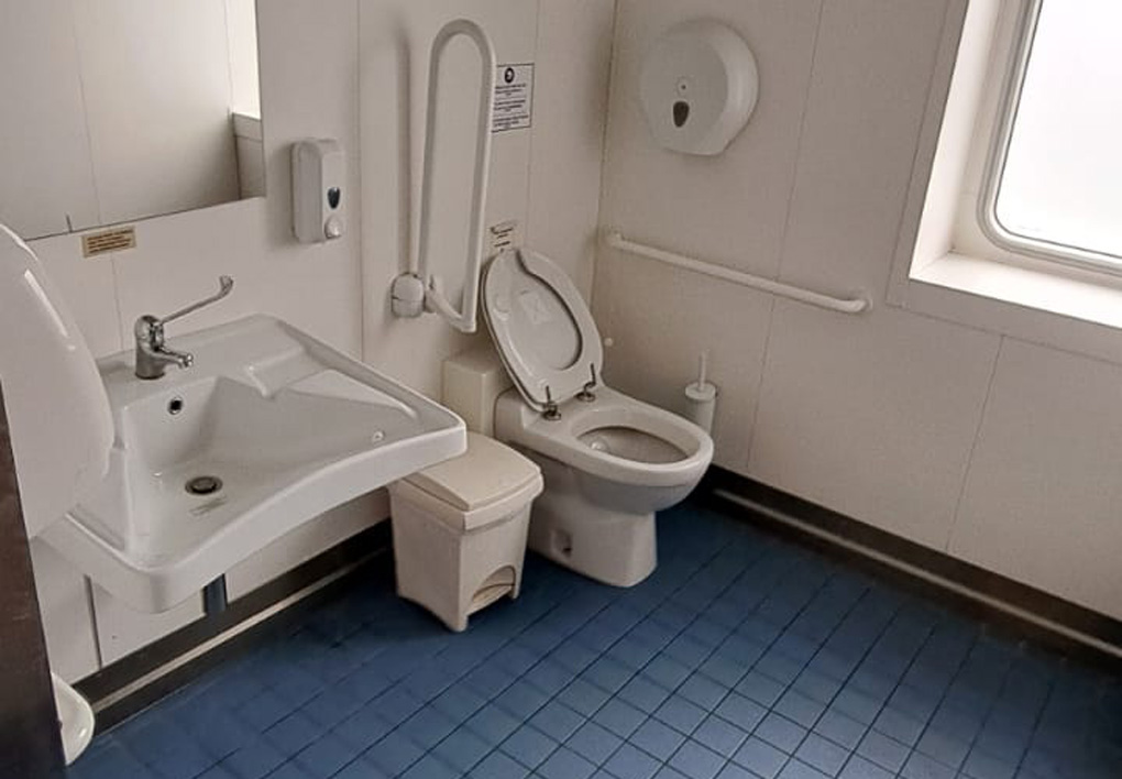 un ampio bagno disabili, con piastrelle blu e pareti bianche. sulle pareti maniglioni di appoggio.