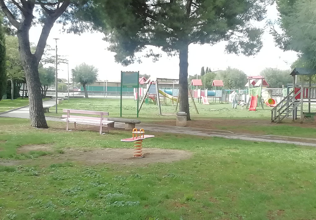 un parco giochi tra gli alberi. Sono presenti panchine all'ombra