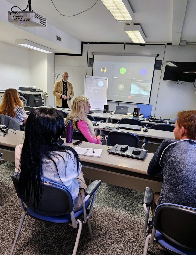 Il presidente di Bandiera Lilla Roberto Bazzano tiene una lezione di fronte a persone in classe e persone collegate, proiettate su uno schermo alle sue spalle