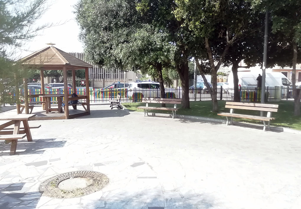 Un gazebo in legno in uno spiazzo del parco, con panchine e alberi intorno ad esso