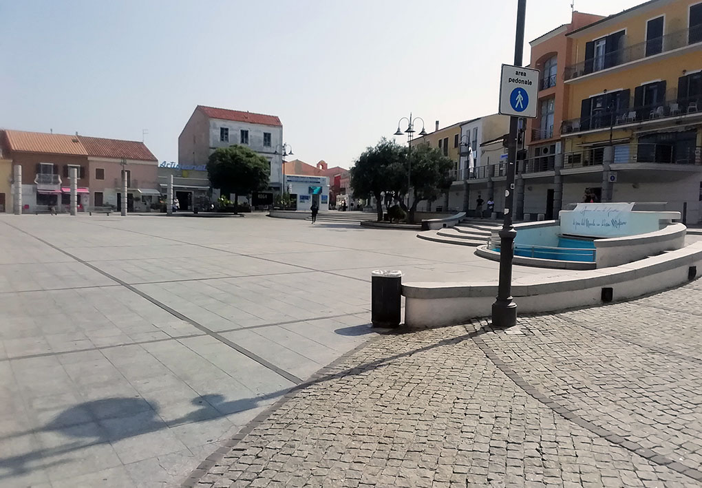 una piazza pianeggiante con ai lati alcuni muretti e alberi. In accesso si nota una rampa lastricata con porfido