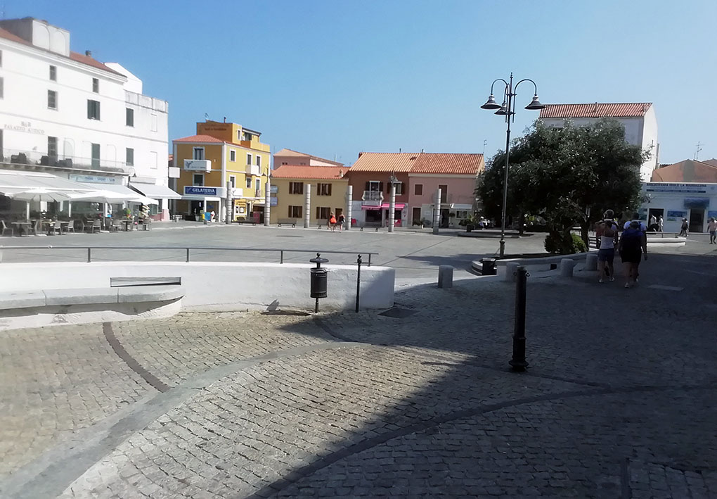 da una zona leggermente rialzata e all'ombra, con pavimentazione in porfido, la foto inquadra una piazza pianeggiante e assolata