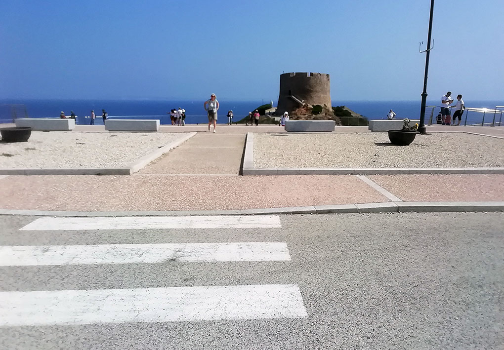 un punto panoramico affacciato sulla punta estrema dell'isola. Il marciapiede è raccordato alle strisce pedonali da una piccola rampa. Si intuisce che la terrazza panoramica è a un livello inferiore rispetto la strada