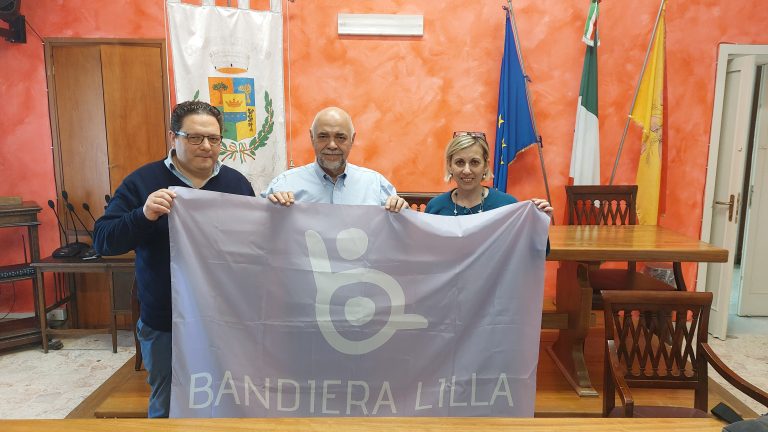Il presidente di Bandiera Lilla posa con la bandiera e i rappresentanti dell'Amministrazione di Letojanni