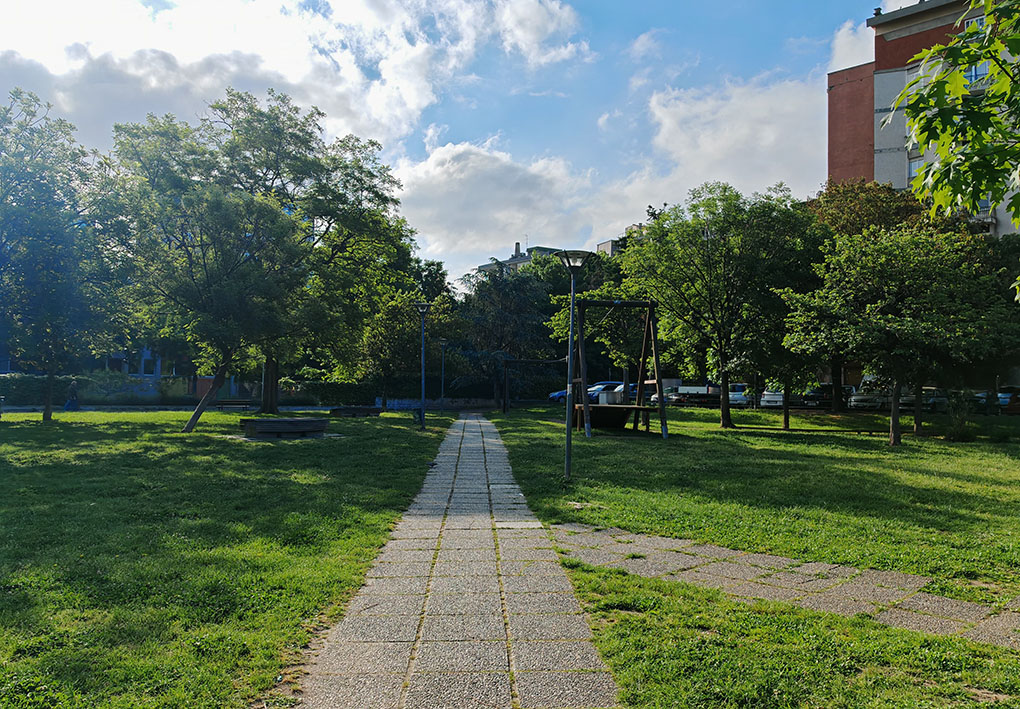 un sentiero pavimentato attraversa un prato con alberi e un'imponente struttura gioco