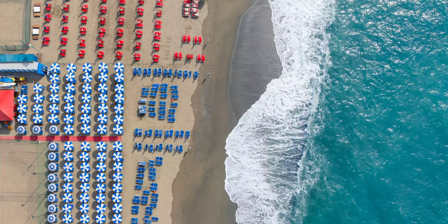 una fotografia dal drone riprende gli ombrelloni sulla spiaggia e le onde che si infrangono su di essa