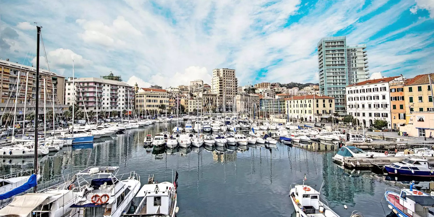 una suggestiva inquadratura del porto di savona. Imbarcazioni sono ancorate lungo tutto il perimetro e sul fondo si vedono i palazzi della città