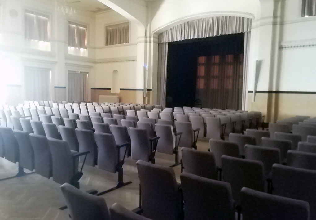 Sala di teatro con moltre file di poltroncine, stanza ampia e illuminata