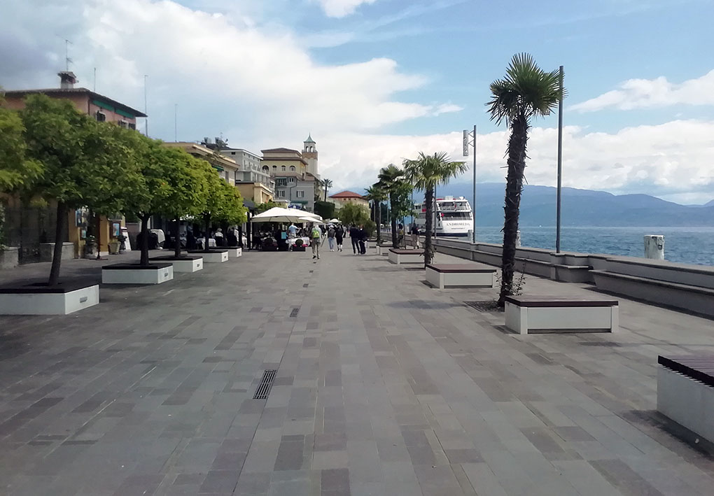 Lungolago pedonale con pavimentazione rugosa con alberi e bar presenti