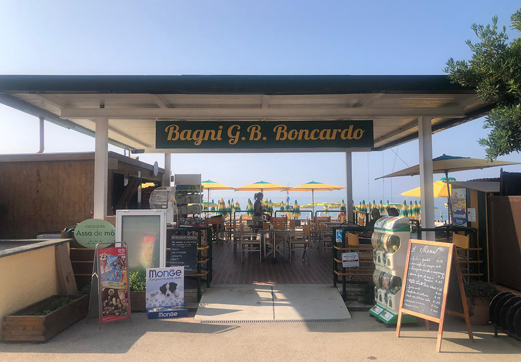 L'entrata dei bagni. Dal lungomare una passerella permette di accedere alla zona bar. Al di là della terrazza, gli ombrelloni della spiaggia.
