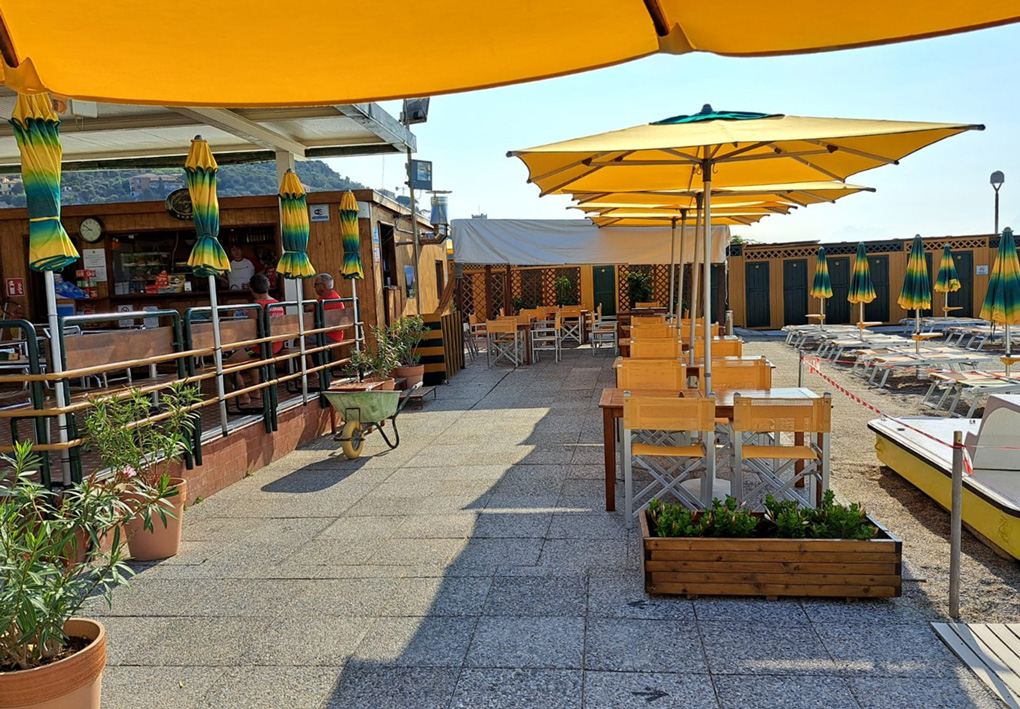 terrazza lastricata di accesso. Ombrelloni regalano un po' di ombra ad alcuni tavolini