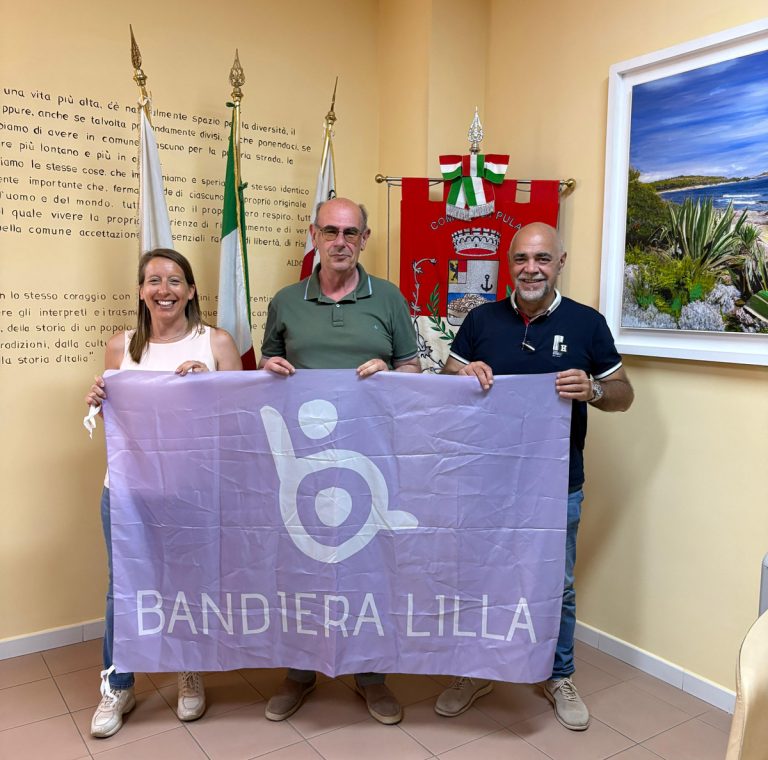 Il presidente di Bandiera Lilla posa con il sindaco e l'Assessore di Pula, mostrando la Bandiera Lilla