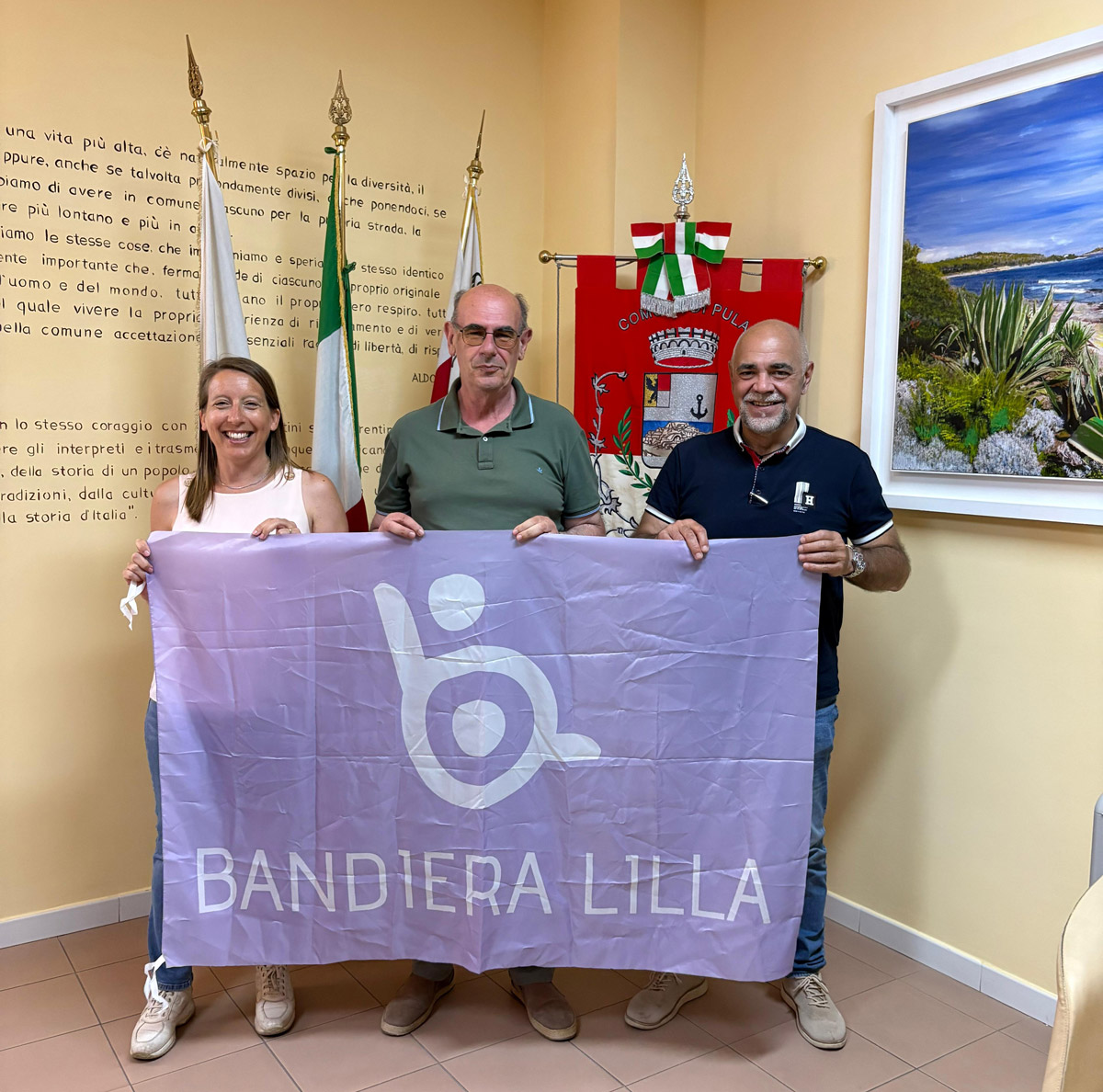 Il presidente di Bandiera Lilla posa con il sindaco e l'Assessore di Pula, mostrando la Bandiera Lilla