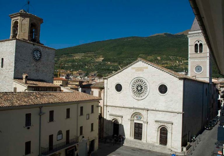 Piazza principale del borgo, su cui si affacciano edifici in pietra. Sullo sfondo colline verdeggianti e un cielo terso
