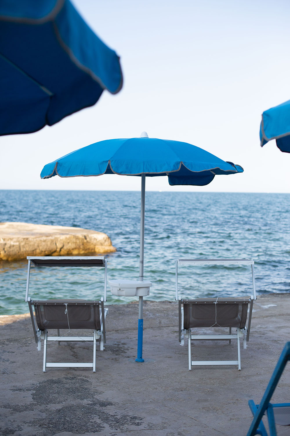 due lettini sotto un ombrellone si affacciano sul mare limpido, increspato di lievi onde