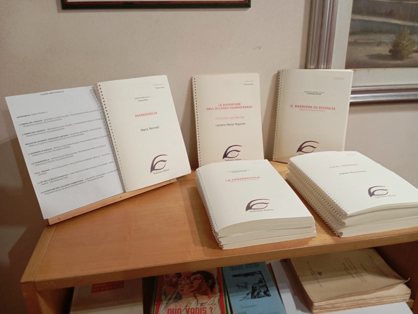 Mensole con documenti rilegati a spirale, uno aperto, titoli visibili e libri disposti sotto.