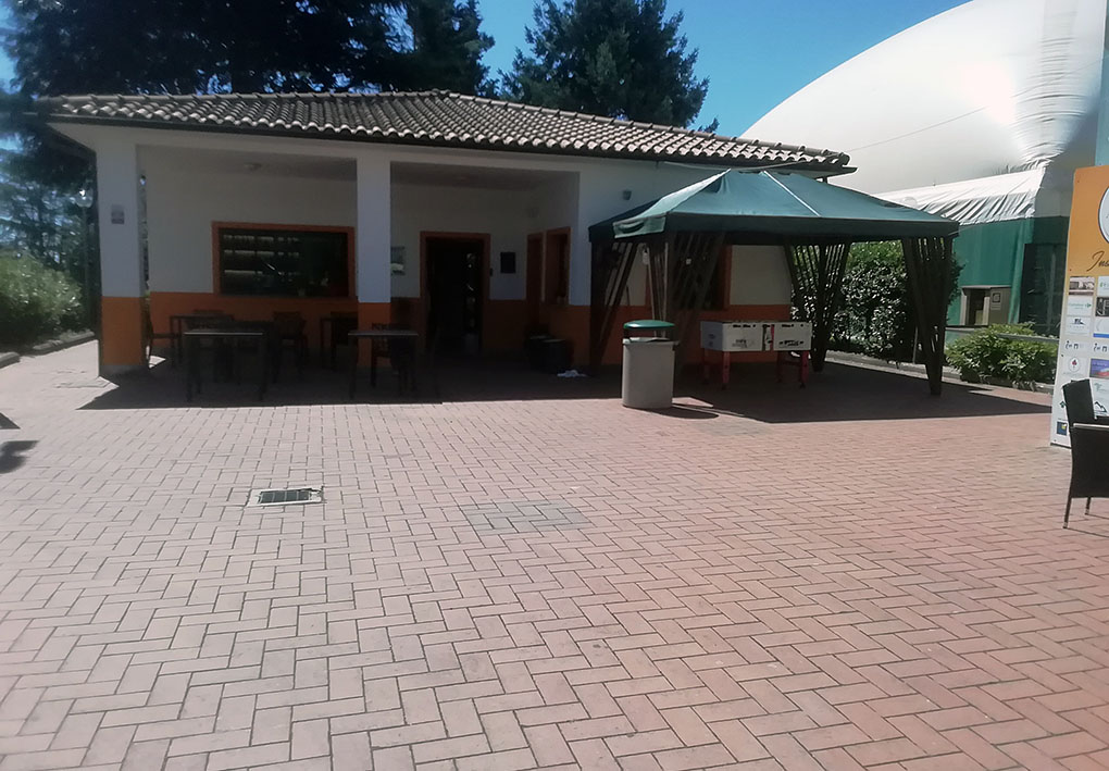 Edificio con tetto in tegole e cortile pavimentato in mattoni rossi, con tavoli e sedie.
