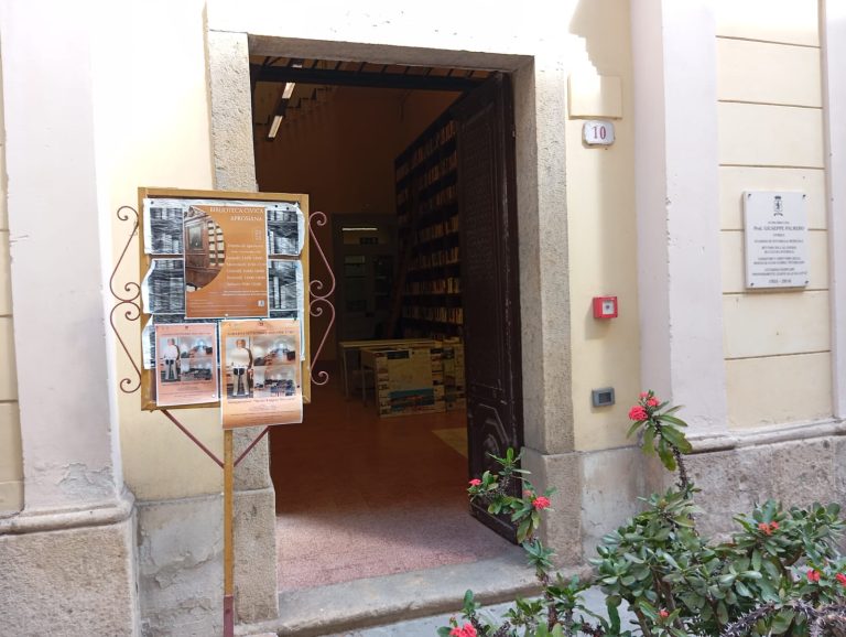 Ingresso edificio con muro in pietra. Porta senza soglia e cartello informazioni all'ingresso.
