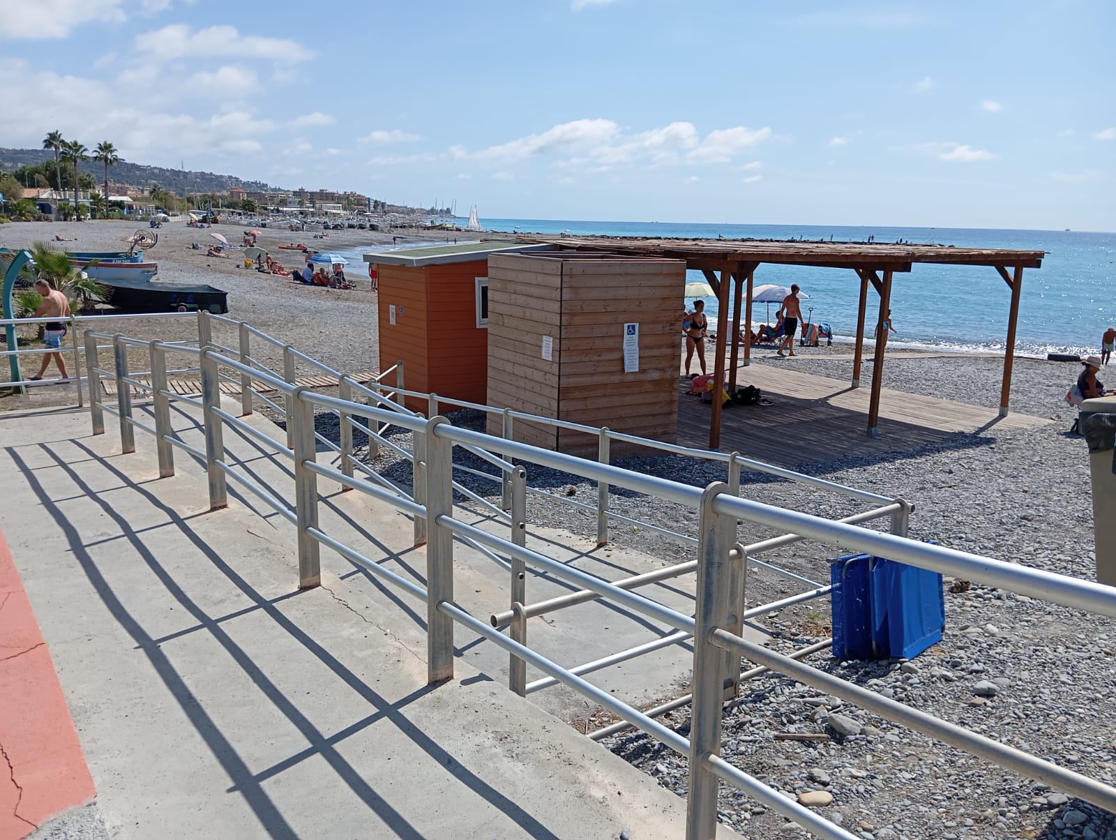 Spiaggia libera attrezzata con ciottoli, passerella per accedere alla spiaggia e struttura in legno.