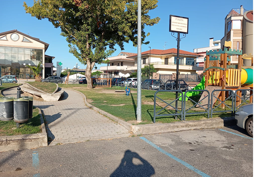una zona in erba con giochi per bambini fiancheggia un vialetto al centro di una piazza
