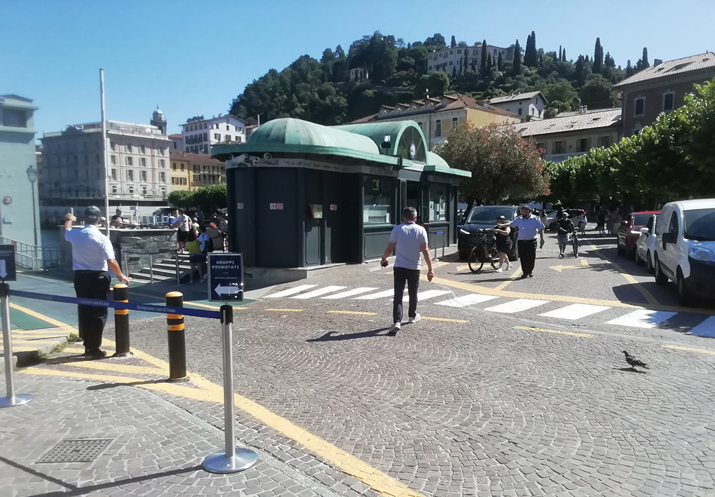 una bassa costruzione in stile liberti si affaccia su una piazza lastricata. Macchine in coda attendono il turno di imbarcare, di fronte a personale impegnato a dirigerne i movimenti