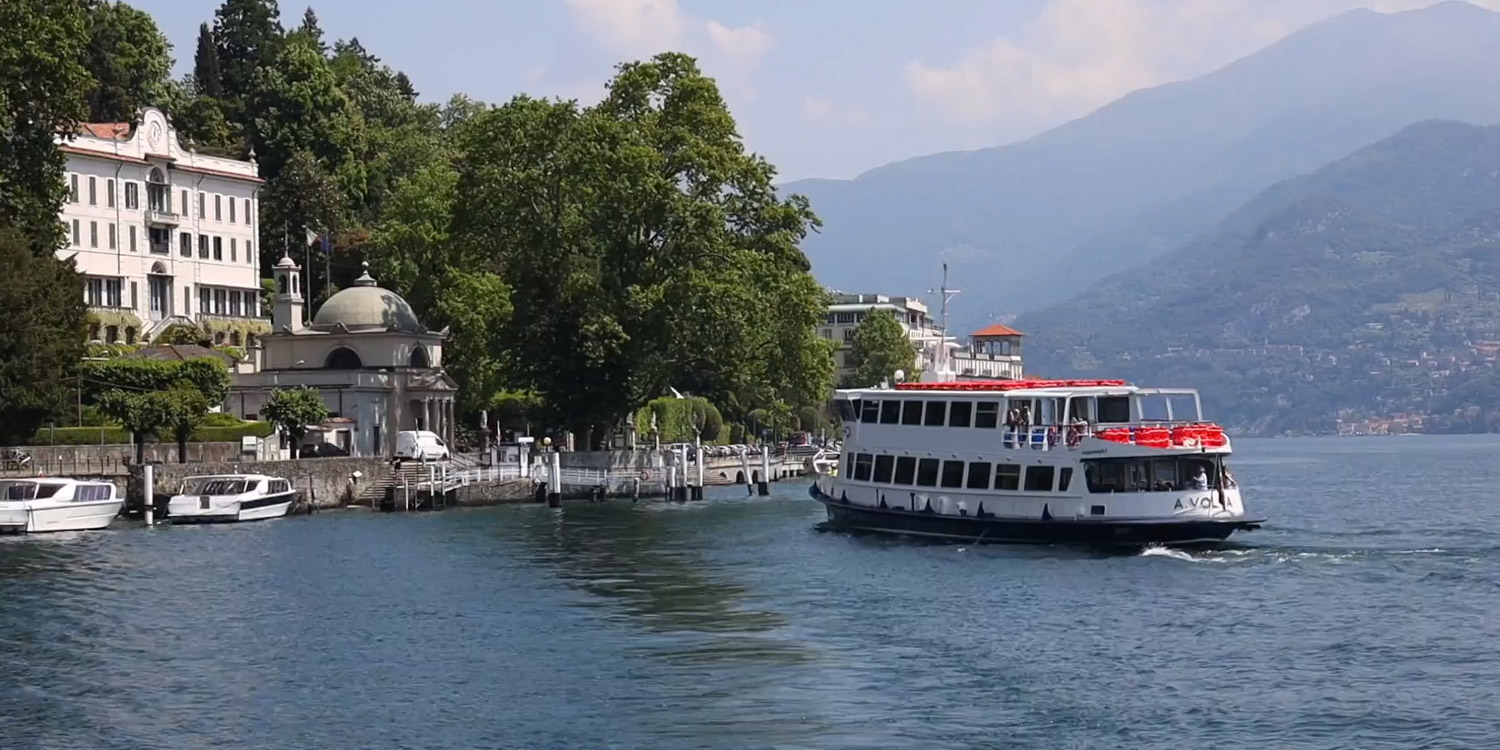 un traghetto si avvicina a un molo ricco di alberi, con una imponente e pittoresca villa sulla riva
