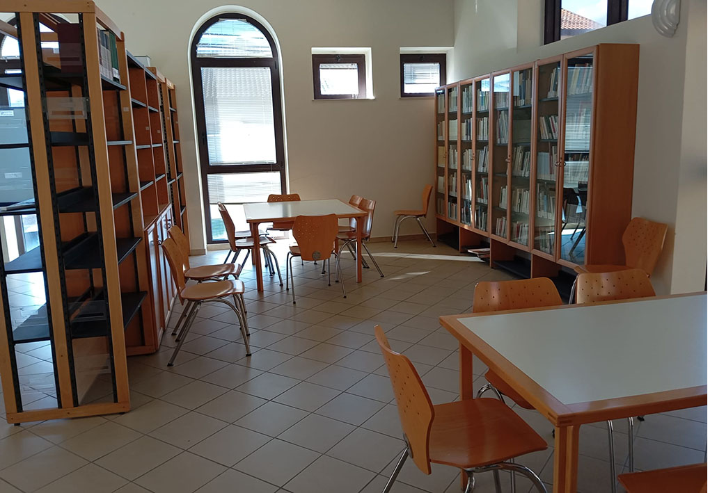 Sala studio con tavoli in legno, sedie e scaffali con libri lungo le pareti.