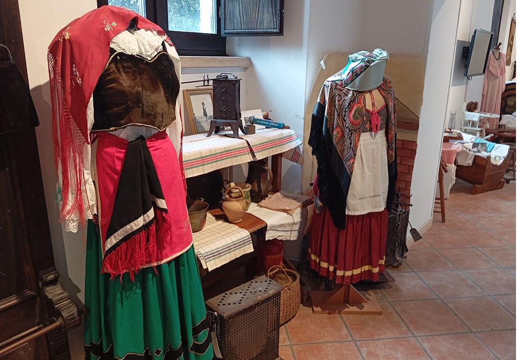 Manichini con abiti tradizionali e tavolo con oggetti domestici storici in ambiente museale.