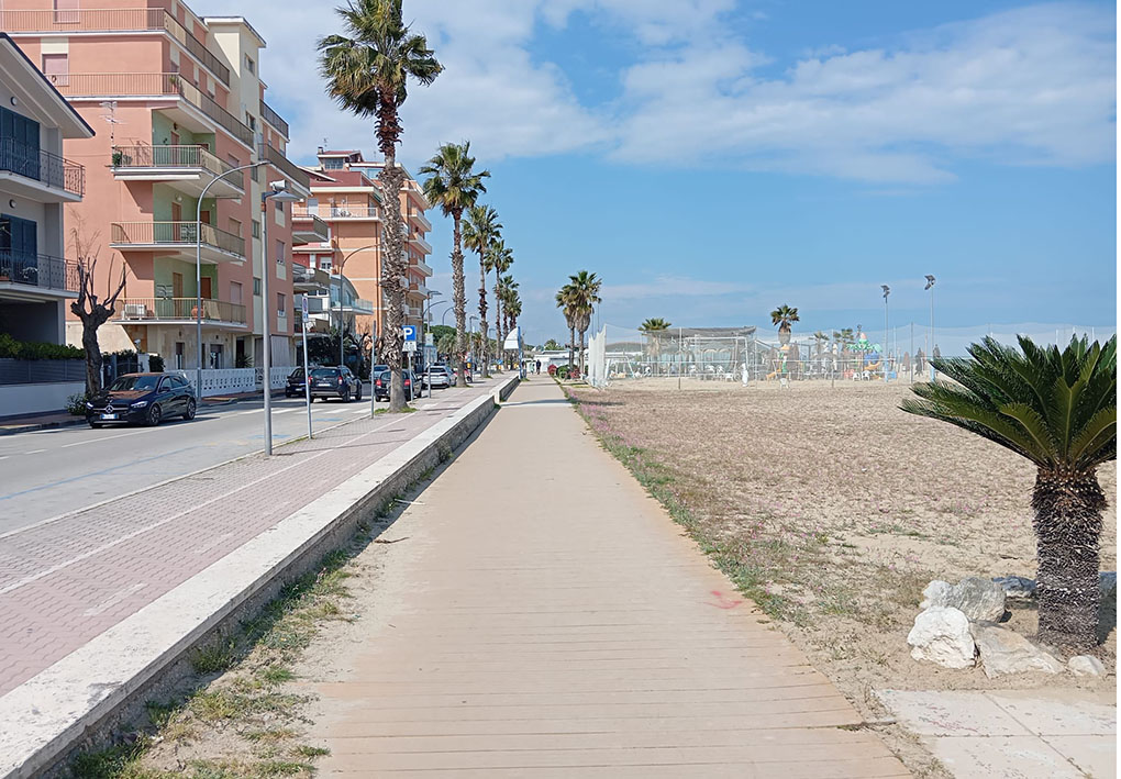 Passeggiata sul mare con palme, edifici residenziali e area sportiva sulla spiaggia