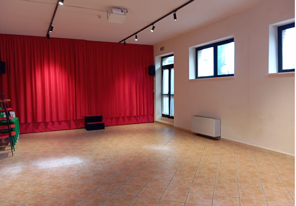 Sala con palco con tende rosse, sedie impilate e impianto audio laterale.