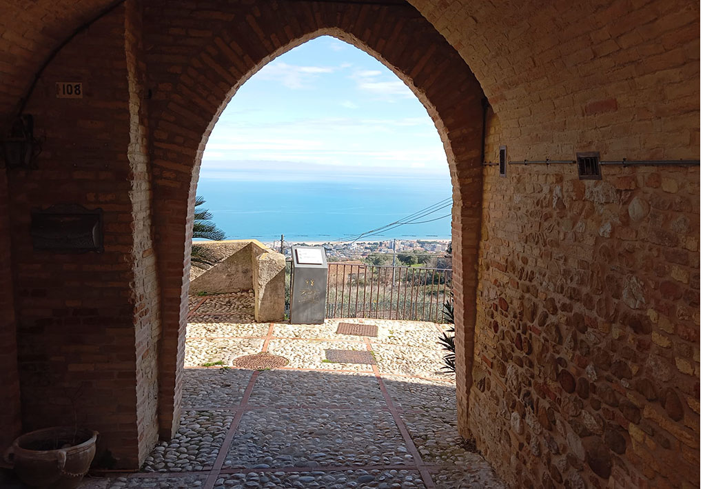Passaggio sotto arco in mattoni con pavimento in ciottoli e vista panoramica sul mare.