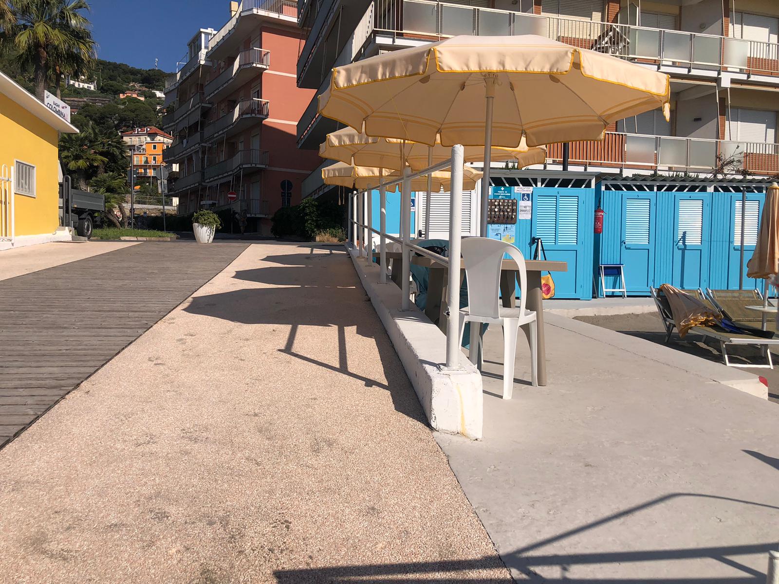 Spazio esterno con tavoli ombreggiati e cabine colorate, collegati da percorsi larghi e regolari adatti anche a persone con mobilità ridotta.