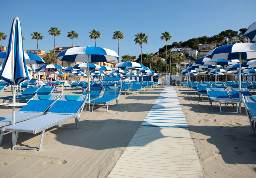Spiaggia attrezzata con lettini e ombrelloni ordinati, raggiungibile tramite passerella pianeggiante che facilita l’accesso